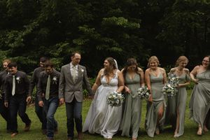 Wedding party in sage green dresses and gray suits stands in line formation outdoors.