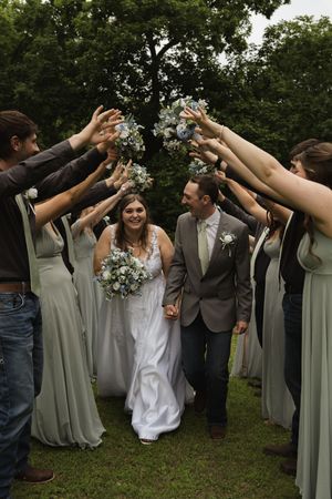 Wedding party forms tunnel with raised arms while couple walks through during outdoor celebration.