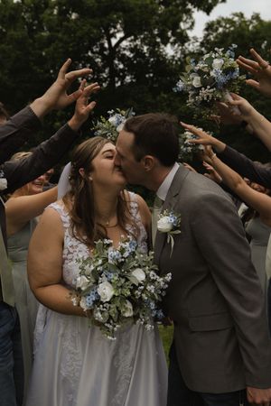 Wedding couple shares romantic moment under archway of raised arms during outdoor celebration.