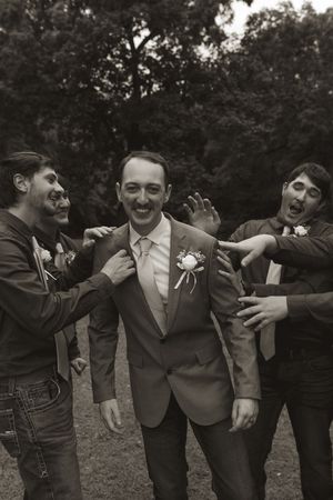 Groomsmen in gray suits playfully pose together outdoors during wedding photo session.