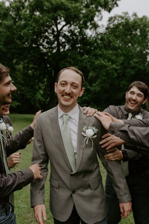 Wedding party members share candid laughs while taking photos in a garden setting.