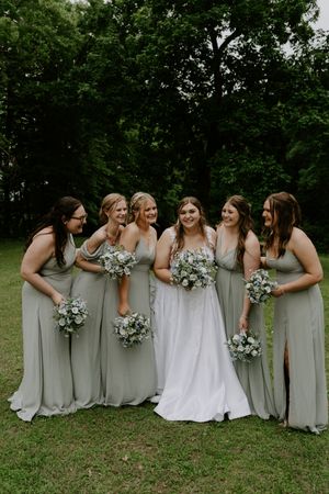 Bridesmaids in sage green dresses line up with bride in white for a fun group photo.