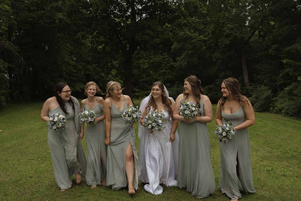 Wedding party in sage green dresses poses together on grass.