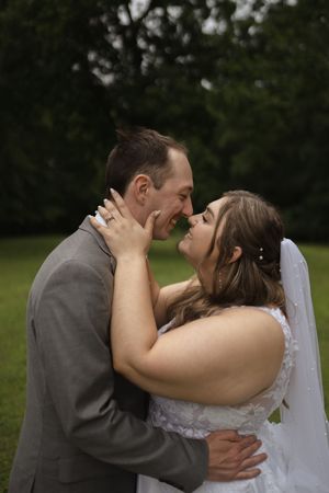 Romantic wedding kiss between couple in grey suit and white dress outdoors.