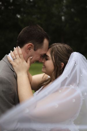 Intimate wedding moment captured through flowing white veil outdoors.