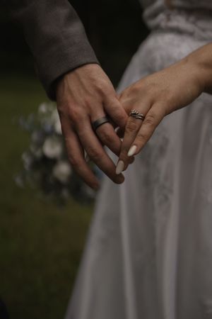 Detail shot of wedding bands on couple's hands against white dress background.