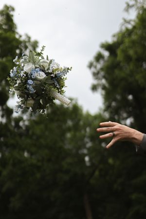 Wedding bouquet being tossed into air against green trees.