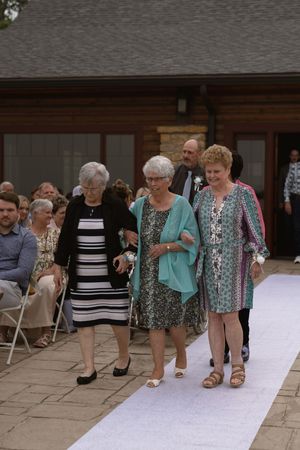 Wedding guests walking down a white aisle runner during an outdoor ceremony.