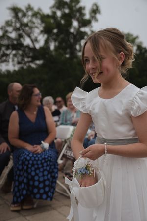 Flower girl in white dress with gray sash explores her dress pockets during wedding festivities.