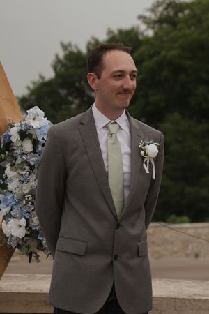 Groom in a grey suit with mint green tie poses during outdoor wedding photography session.