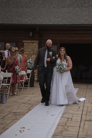 Wedding ceremony setup with white aisle runner and chairs on stone patio.