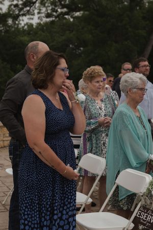 Wedding guests in blue and mint colored dresses seated at an outdoor ceremony venue.