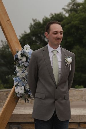 Wedding ceremony setup featuring wooden arch decorated with white and blue floral arrangements.