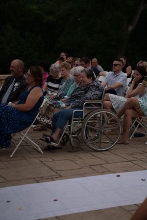 Wedding guests seated in folding chairs on a stone patio during an outdoor ceremony.