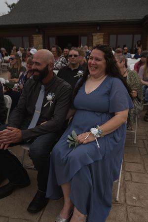 Wedding party members in blue dresses seated during outdoor ceremony.