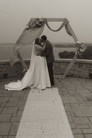Black and white wedding photo showing couple embracing on stone patio with flowing veil.