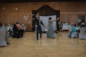 Wedding celebration in rustic wood-paneled reception hall with guests seated at decorated tables.