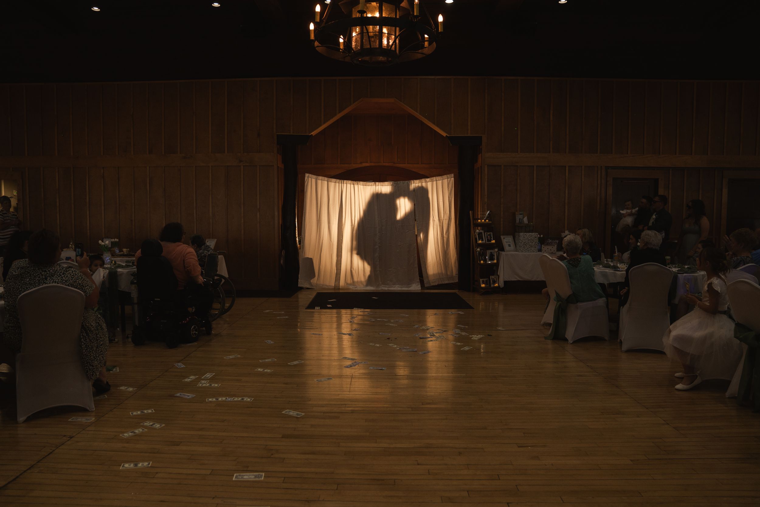 Wedding guests seated in rows of chairs at an indoor reception venue with dramatic lighting.