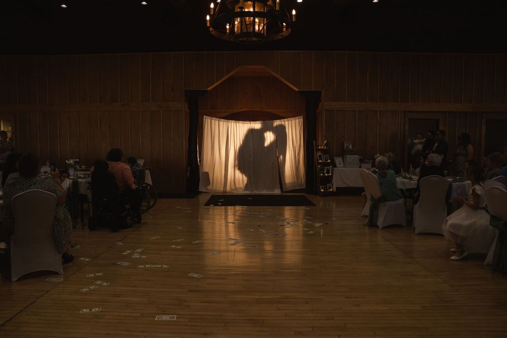 Wedding guests seated in rows of chairs at an indoor reception venue with dramatic lighting.