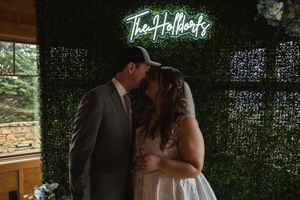 A dimly lit indoor wedding venue decorated with greenery walls and neon signage.