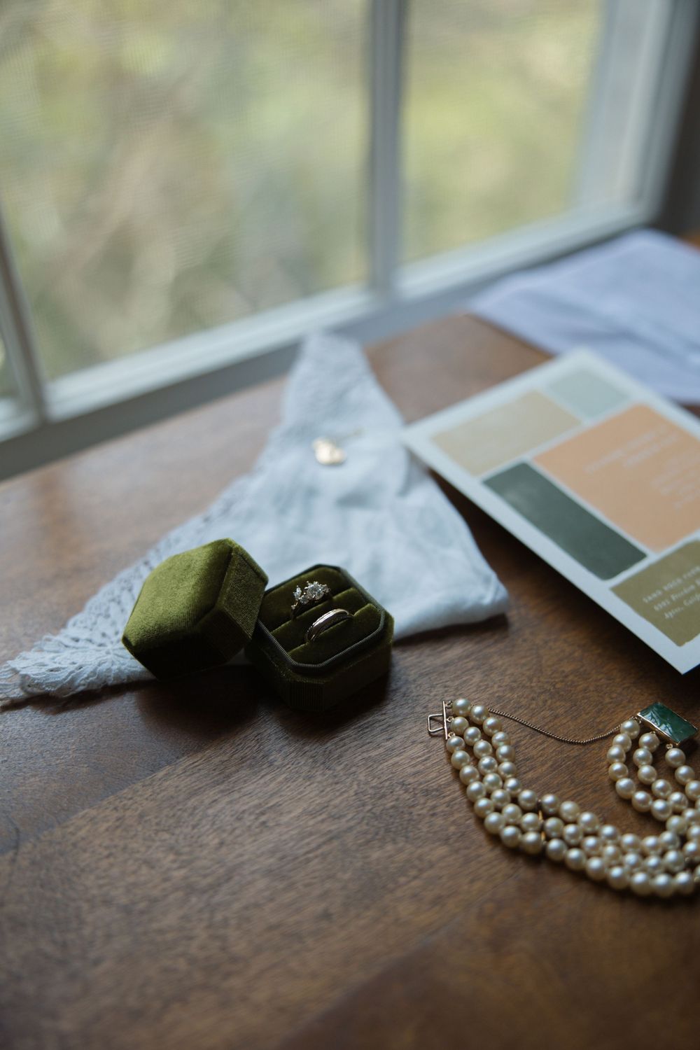 Wedding detail flat lay with pearl necklace, rings, handkerchief, and invitation