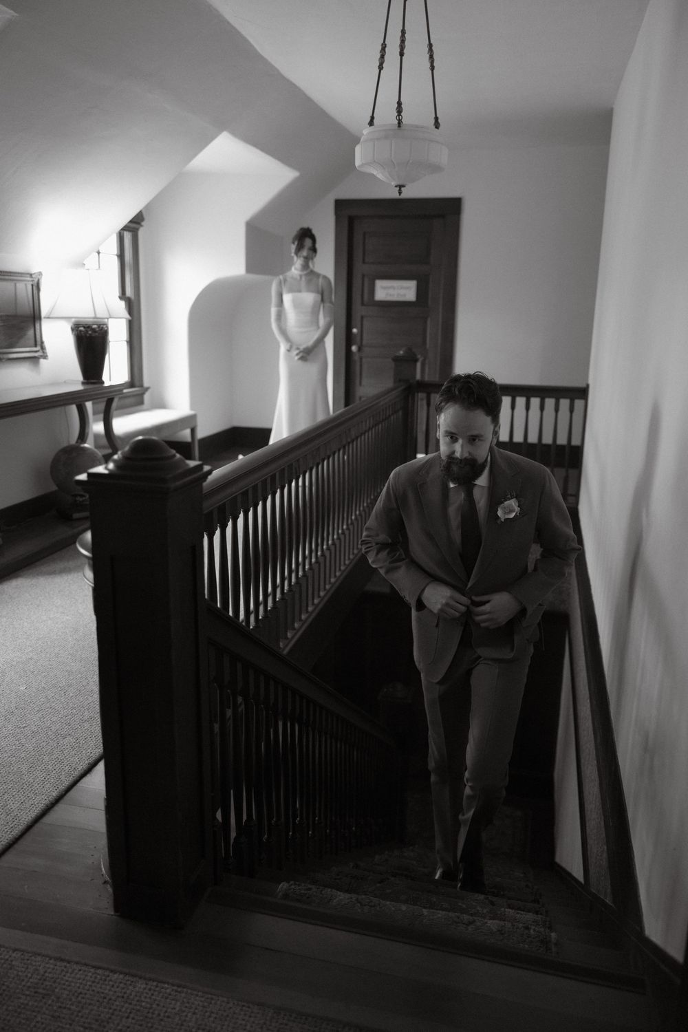 Black and white photo of groom approaching bride for their first look on the stairs