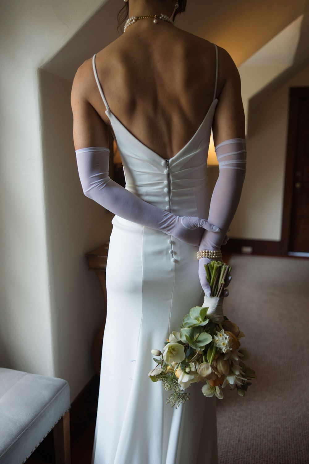 Detail of bride’s minimalist gown with sheer gloves and garden-style bouquet