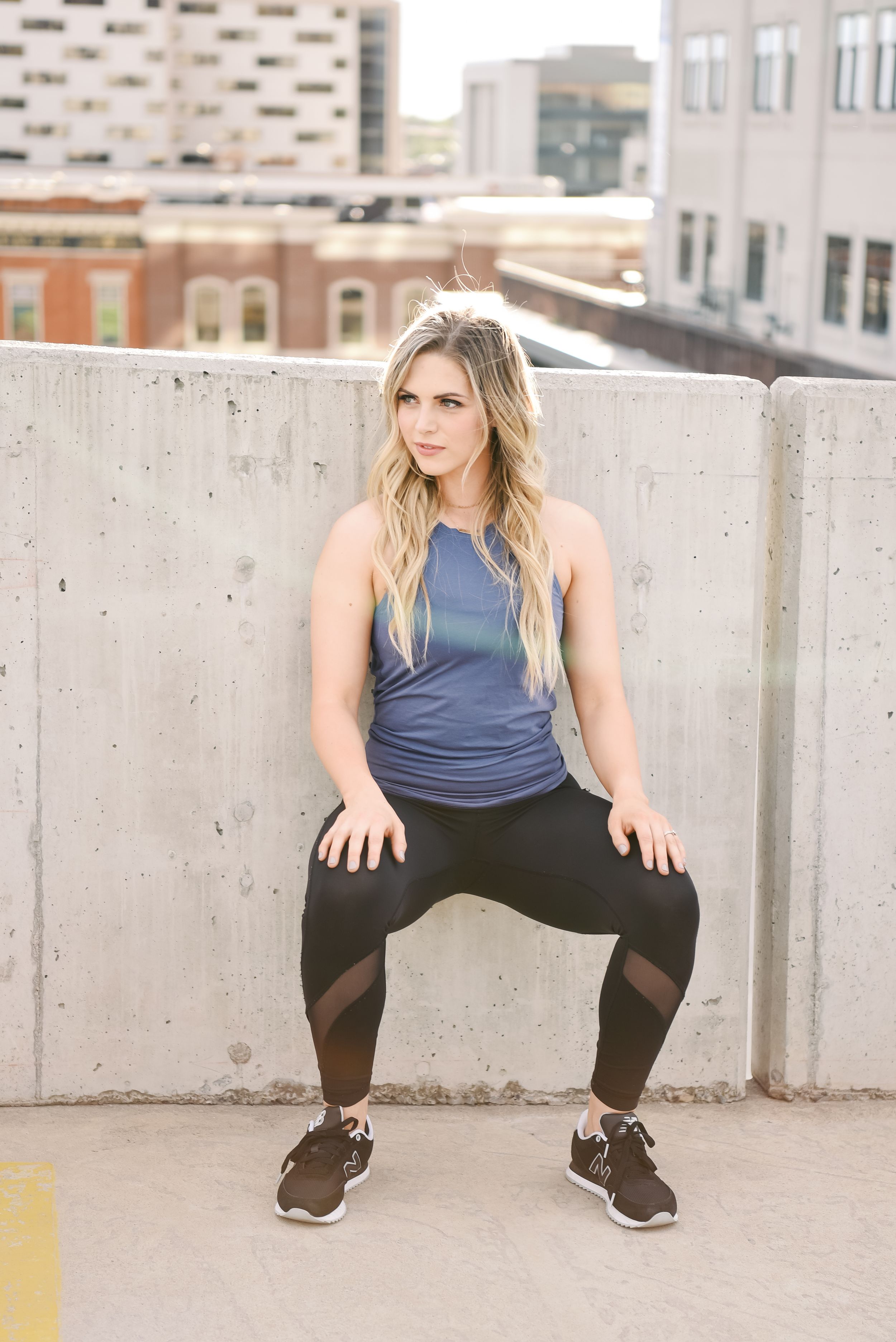 Person in athletic wear demonstrates a squat stance against concrete wall in urban setting.