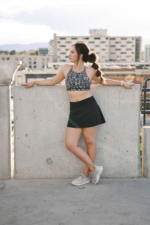 Woman in athletic wear stretches on concrete wall against urban backdrop during workout session.