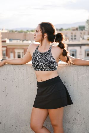 Athletic figure in patterned crop top and black skirt poses on rooftop with city backdrop.