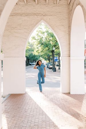 Bright arched colonnade frames a figure in denim jumping through sunlit brick courtyard on urban street.