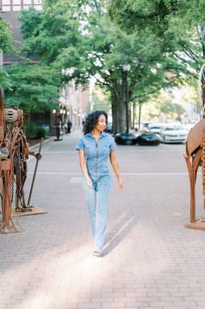 Person wearing denim outfit walks along brick path with bronze sculptures lining both sides of the walkway.