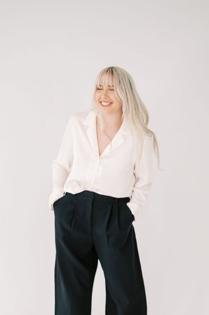 Person in casual business attire with white blouse and black trousers posing against light background.