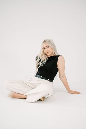 A person in a black sleeveless top and white pants poses gracefully against a white backdrop in a fashion photography series.