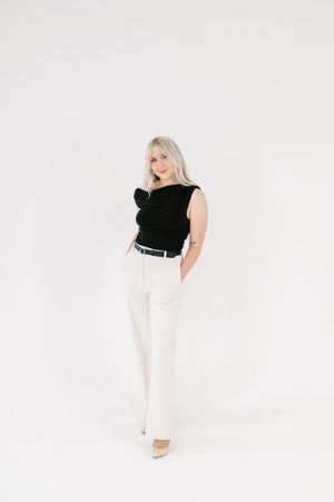 Plus size fashion model wearing a black sleeveless top and white pants poses against white background in studio setting.