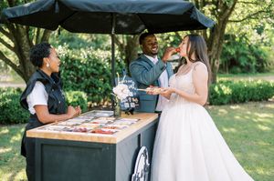 Guests enjoy refreshments at an outdoor catering station with a black canopy in a garden setting.