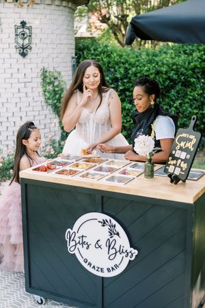A mobile dessert cart labeled 'Bits & Bites Grazing Bar' displays treats while guests sample offerings outdoors.