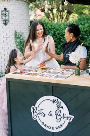 Friends share laughter and conversation while enjoying appetizers at an outdoor table with a restaurant logo visible.