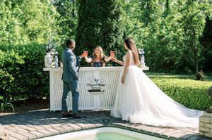 An outdoor wedding ceremony takes place in a lush garden setting with a white decorative altar and elegant floral arrangements.