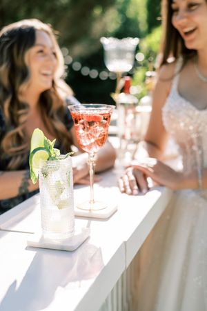 Elegant cocktail glasses with colorful drinks and garnishes arranged on a white table at an outdoor celebration.