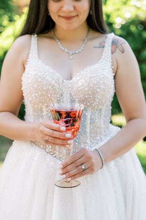 A close-up view of someone wearing a sparkling white wedding dress holding a rose gold cocktail.