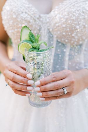Close-up of hands holding crystal cocktail glasses decorated with lime and mint garnishes.