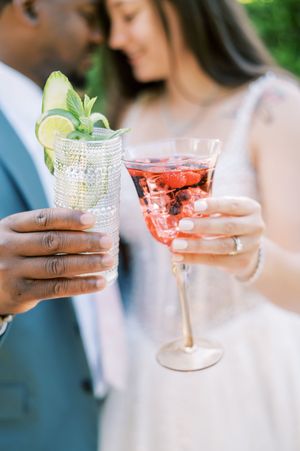 Close-up of cocktail glasses with garnishes being held during an outdoor wedding celebration.