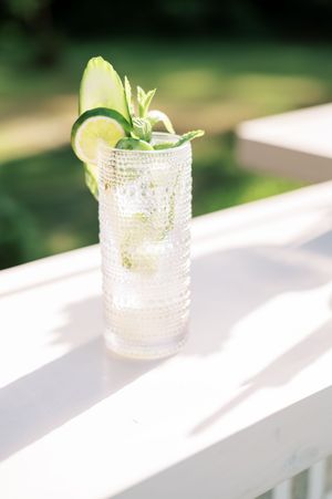 A crystal textured cocktail glass with a lime garnish sits on a white ledge casting dramatic shadows.