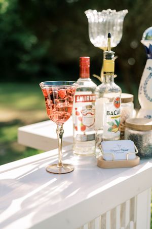 Artfully arranged cocktail glasses and spirits bottles on a white outdoor bar in natural sunlight.