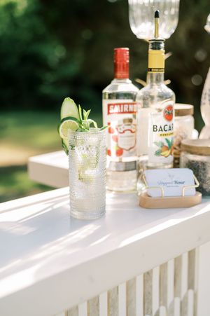Cocktail bar setup on white railing with Bacardi and Smirnoff bottles and garnished drinks.