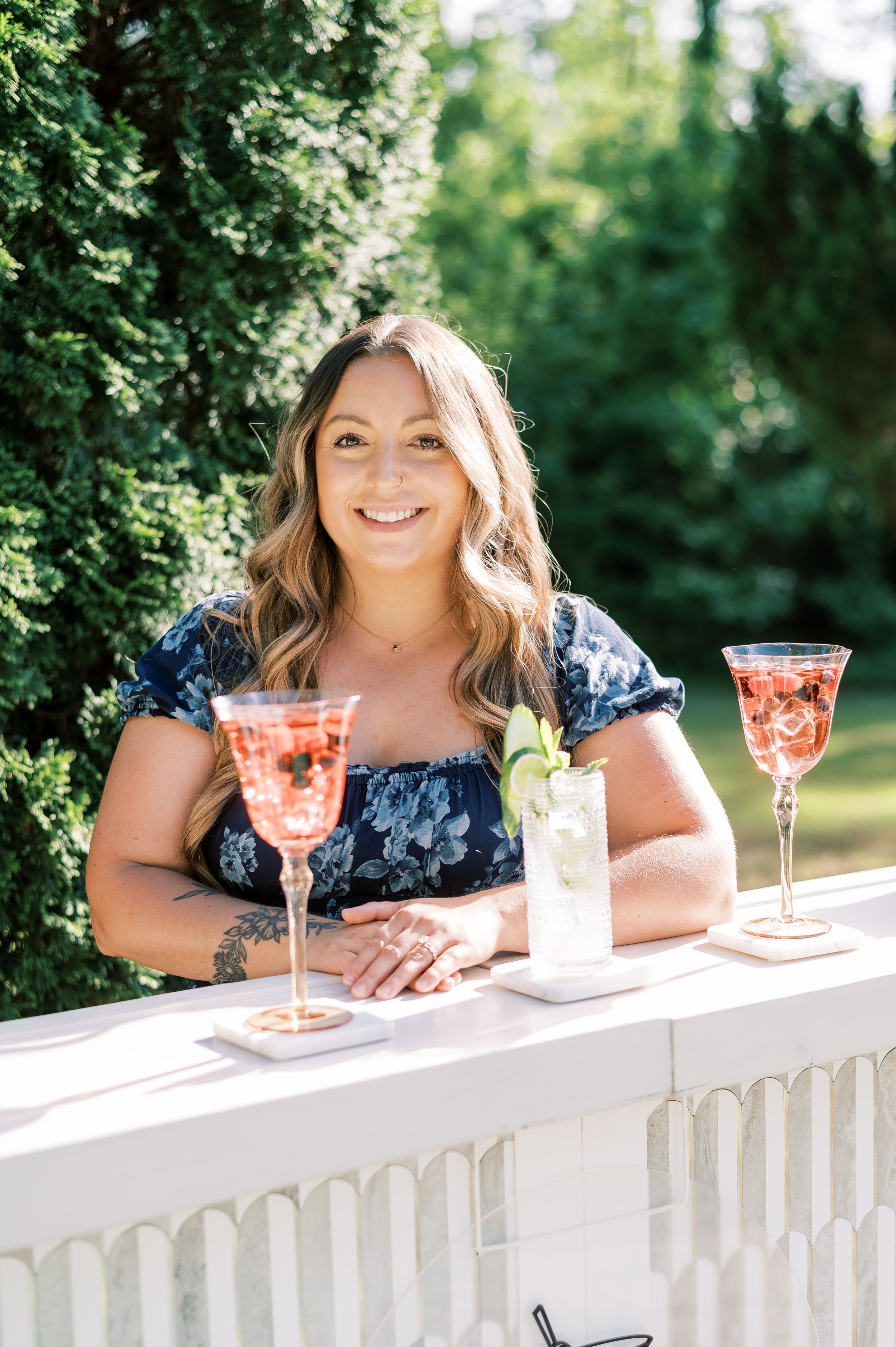 Wedding guests leaning on a white picket fence with pink cocktails and enjoying the outdoor setting.