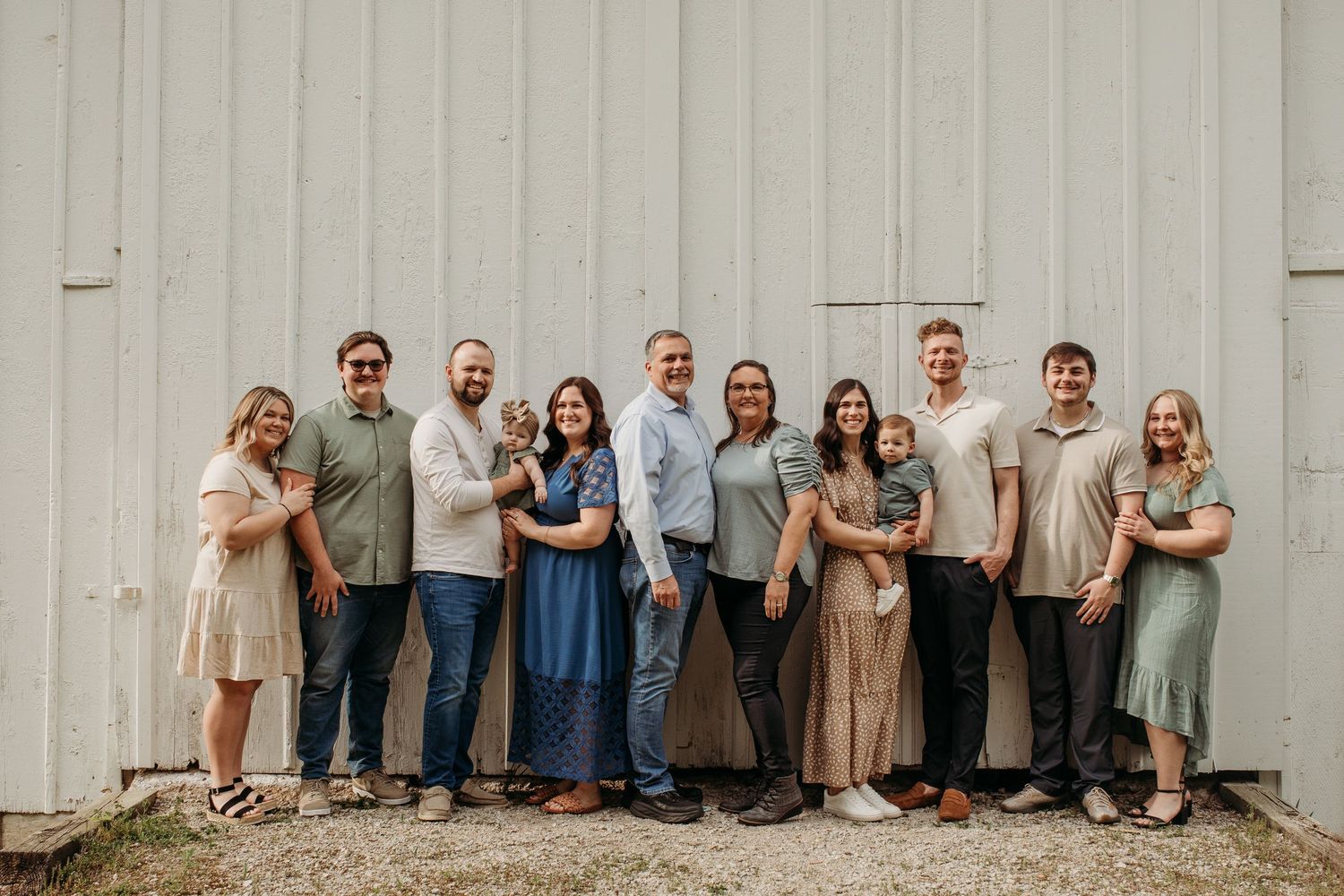 Large extended family group photo lined up against rustic white barn wall.