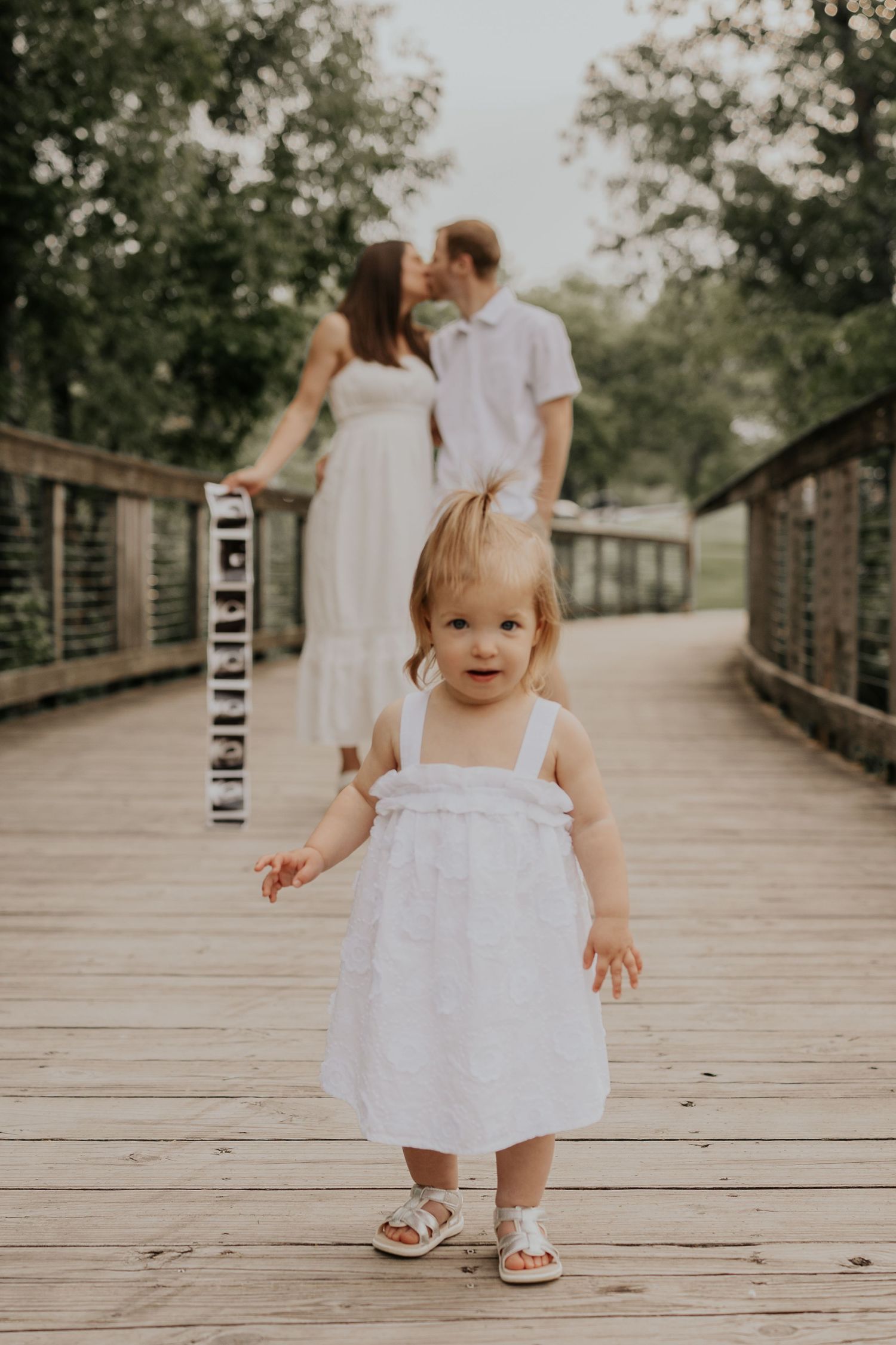 A sequence of photos shows a little girl in a white dress walking and playing on a wooden bridge walkway outdoors.