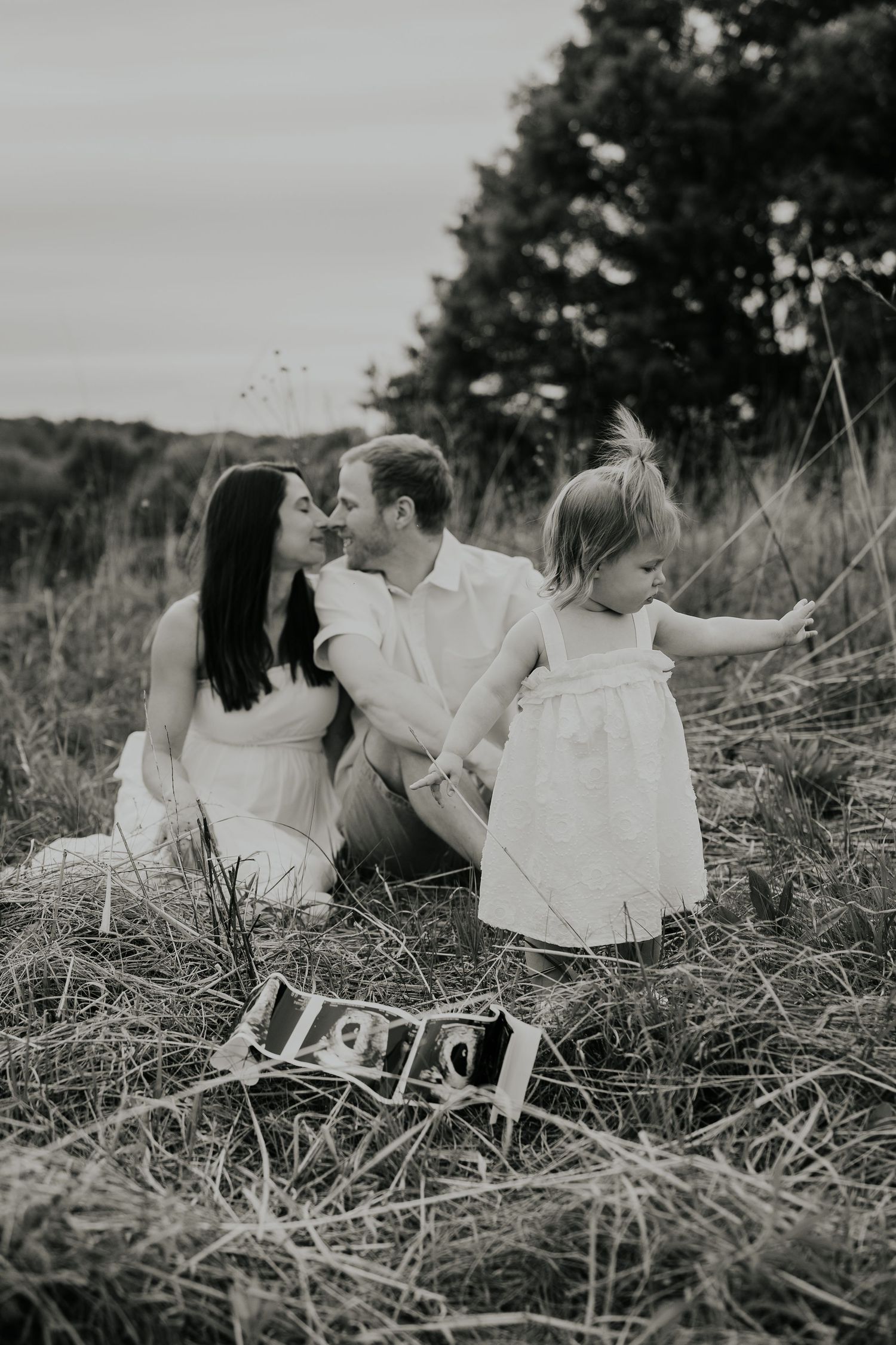 Black and white photo of family sitting in grassy field with a small sign visible in foreground.